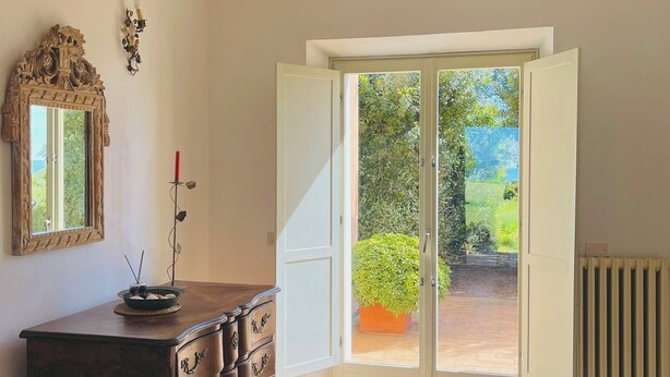 A room with a wooden dresser, a mirror, a wall sconce, and a sliding glass door leading to a garden. - Dune (Montalto di Castro)