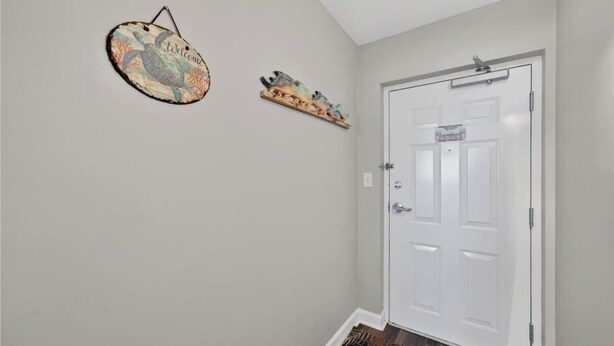 A hallway with a white door, a welcome sign, and a small shelf with decorative items. - Oceanfront Elegance at Blue Water Keyes 604 (Myrtle Beach)