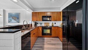 A modern kitchen with wooden cabinets, a black refrigerator, and a central island with a sink. - Oceanfront Elegance at Blue Water Keyes 604 (Myrtle Beach)
