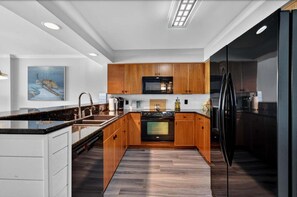 Eine moderne Küche mit Holzschränken, einem schwarzen Kühlschrank und einer zentralen Kochinsel mit Spüle.