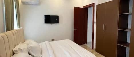 Un dormitorio con cama, televisión, armario y aire acondicionado.