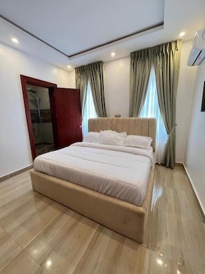 A modern bedroom with a large bed, a wardrobe, and a shower area.