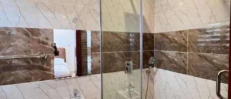 Un baño moderno con ducha envuelta en vidrio, un lavabo y paredes de mármol.