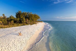 A beach with clear water, a sandy shore, and a person sitting on the sand. - Wonderful 4-bedroom house with AC in tranquil Cape Coral (Cape Coral)