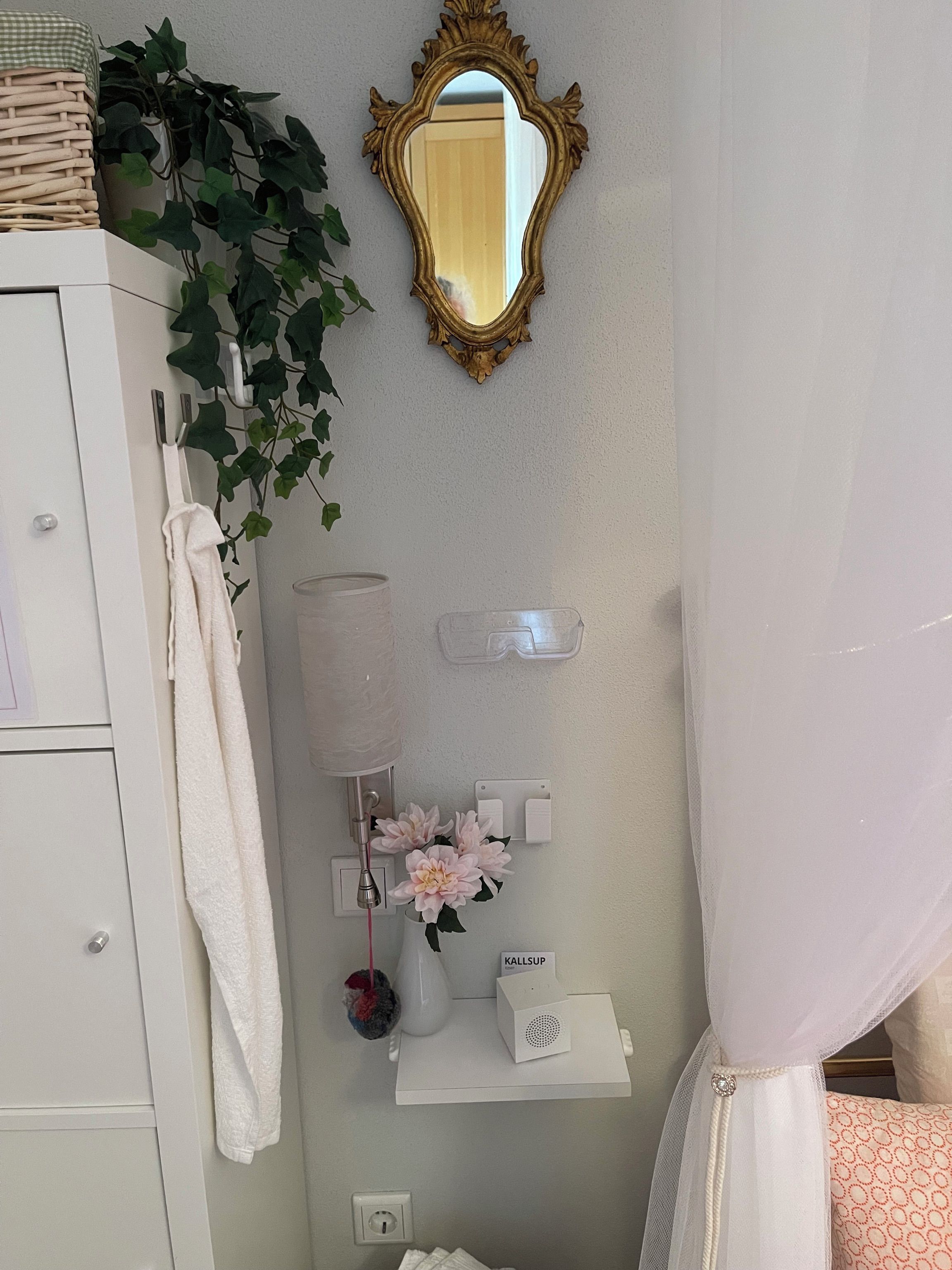 Un bagno con un mobile lavabo bianco, uno specchio, un portascopevoli, una pianta, un vaso con fiori e una tenda da doccia.