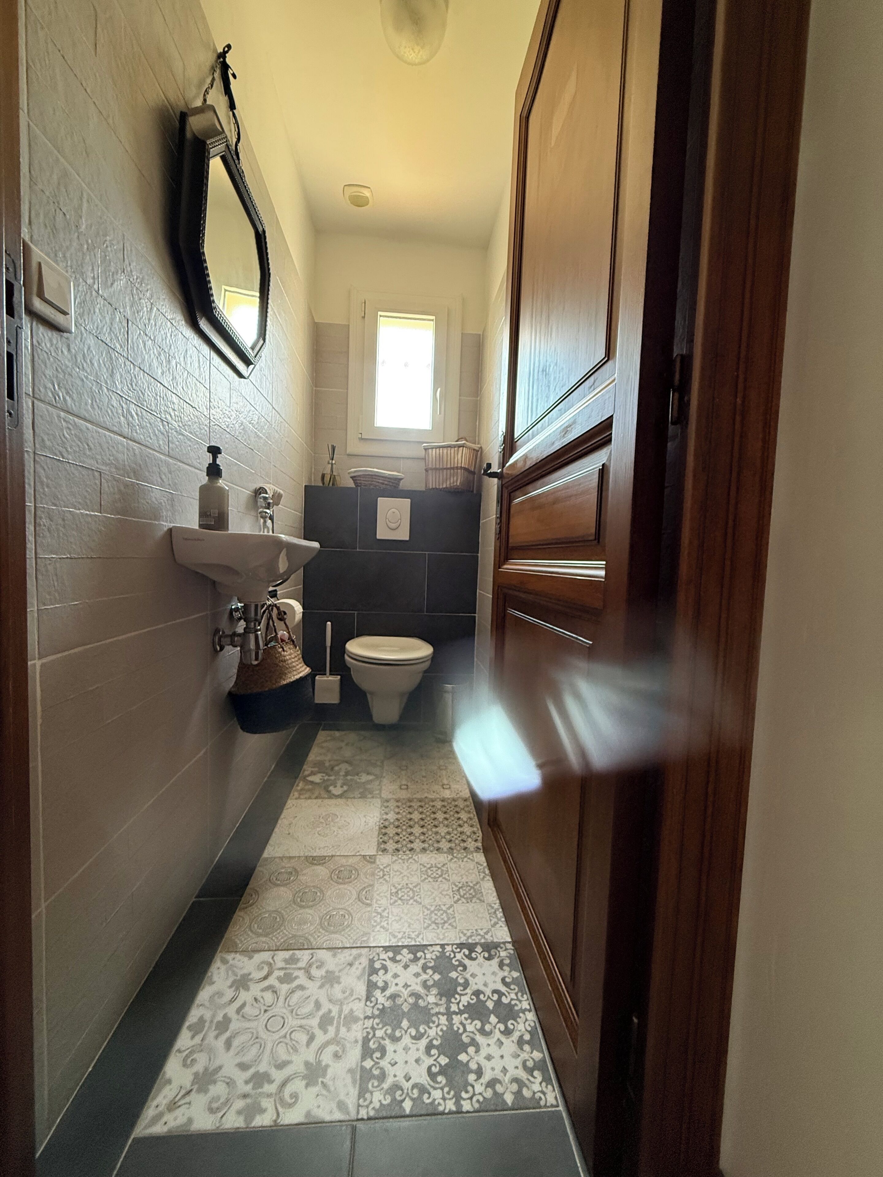 A narrow bathroom with a sink, toilet, and a mirror on the wall.