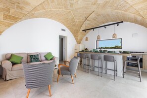 A modern kitchen with a stone arch ceiling, a dining area with a sofa and patterned chairs, and a view through a window. - Onirica Dimora by BarbarHouse (Salve)