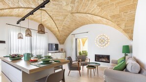 Een ruime woonkamer met een hoog gewelfd plafond, een eettafel gedekt met borden en bestek, een bank met een groen kussen, en een open haard.