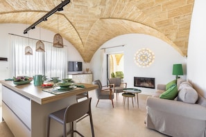 Ein großzügiger Wohnbereich mit hoher, gewölbter Decke, einem Esstisch komplett mit Geschirr und Besteck, einem Sofa mit grünen Kissen und einem Kamin.