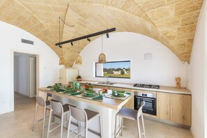 A modern kitchen with a stone ceiling, a central island with seating, and a view of the outdoors through a window. - Onirica Dimora by BarbarHouse (Salve)