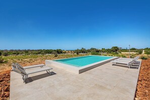 A rectangular swimming pool with a clear blue water surface, surrounded by a paved deck with two lounge chairs on each side. - Onirica Dimora by BarbarHouse (Salve)
