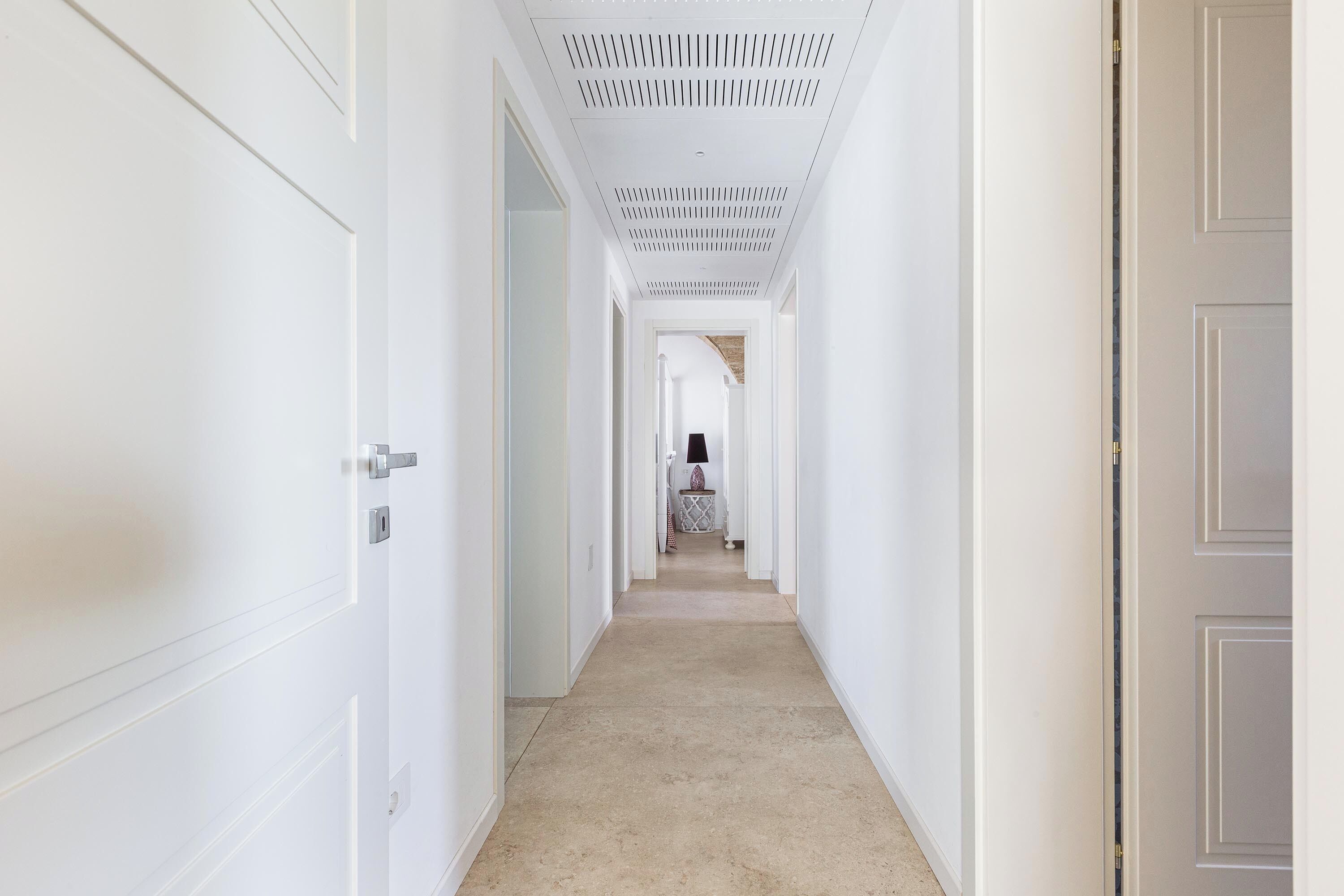 Un corridoio con porte bianche su entrambi i lati, un soffitto decorato e un pavimento tappezzato.