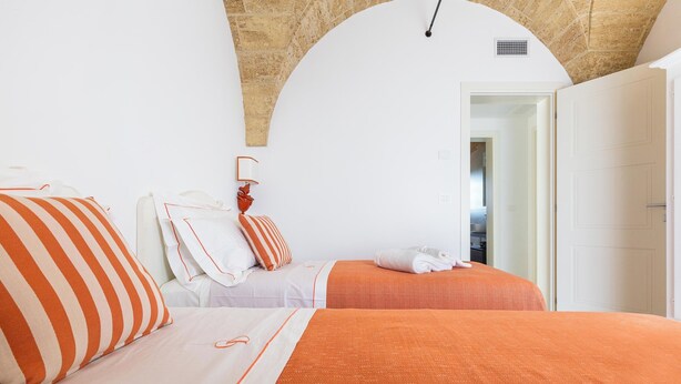 Een hotelkamer met twee bedden, een witte muur, een houten plafond en een deur naar een andere kamer.