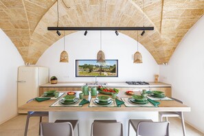 A dining area with a long table set for four, a television mounted on the wall, and a view of a landscape through the window. - Onirica Dimora by BarbarHouse (Salve)