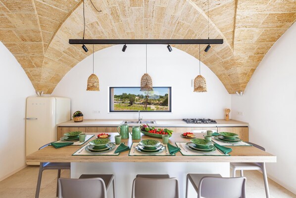A dining area with a long table set for four, a television mounted on the wall, and a view of a landscape through the window. - Onirica Dimora by BarbarHouse (Salve)