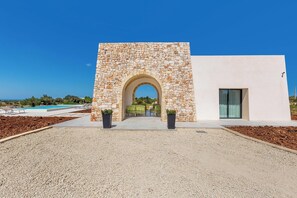 Ein modernes Gebäude mit einer Stein-Fassade, einem Bogenportal und einem Pool im Hintergrund.
