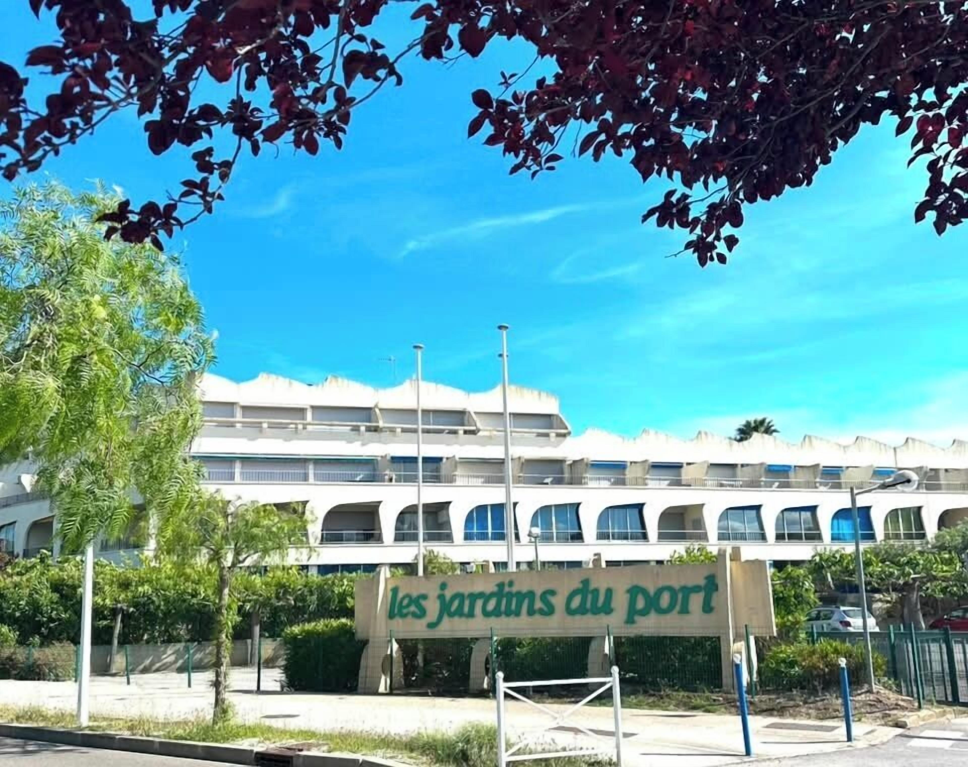 Un edificio con un cartel que dice 'les jardins du port' y un cielo azul despejado.