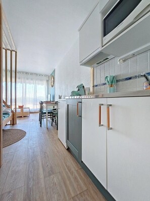 A modern kitchen with white cabinets, a built-in oven, and a window above the sink. - Jardins du Port D3073 – Studio clim, terrasse, parking, Wi-Fi, piscine (Le Grau-du-Roi)