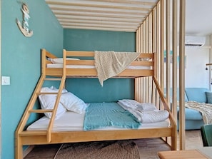 A bunk bed with a wooden frame, a teal wall, and a small table beside it. - Jardins du Port D3073 – Studio clim, terrasse, parking, Wi-Fi, piscine (Le Grau-du-Roi)