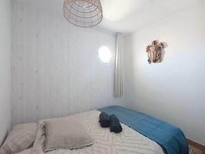Une chambre à coucher comprenant un lit, un luminaire suspendu, une fenêtre ronde et un élément décoratif fixé au mur.