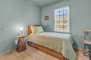 Ein Schlafzimmer mit Bett, Nachttisch, Lampe, Fenster und einem kleinen Bilderrahmen.