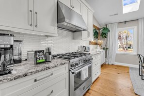 A modern kitchen with white cabinetry, a gas stove, and a coffee maker. - Pool Oasis Near SI Beach | Walk to Parks + Dining (Mount Pleasant)