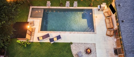 An aerial view of a backyard with a swimming pool, lounge chairs, a fire pit, and string lights.