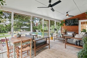A covered patio with a dining table, chairs, and a bench. There are ceiling fans, large windows, and a view of a swimming pool and greenery outside. - Pool Oasis Near SI Beach | Walk to Parks + Dining (Mount Pleasant)