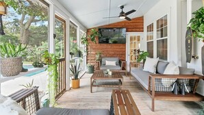 En inglasad veranda med en träbänk, en soffa och ett soffbord. Här finns också krukväxter och utsikt över omgivningen.