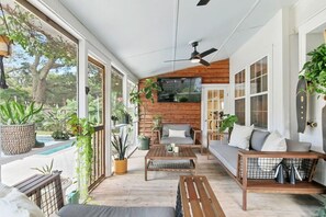 A covered porch with a wooden bench, a sofa, and a coffee table. There are potted plants and a view of the outdoors. - Pool Oasis Near SI Beach | Walk to Parks + Dining (Mount Pleasant)