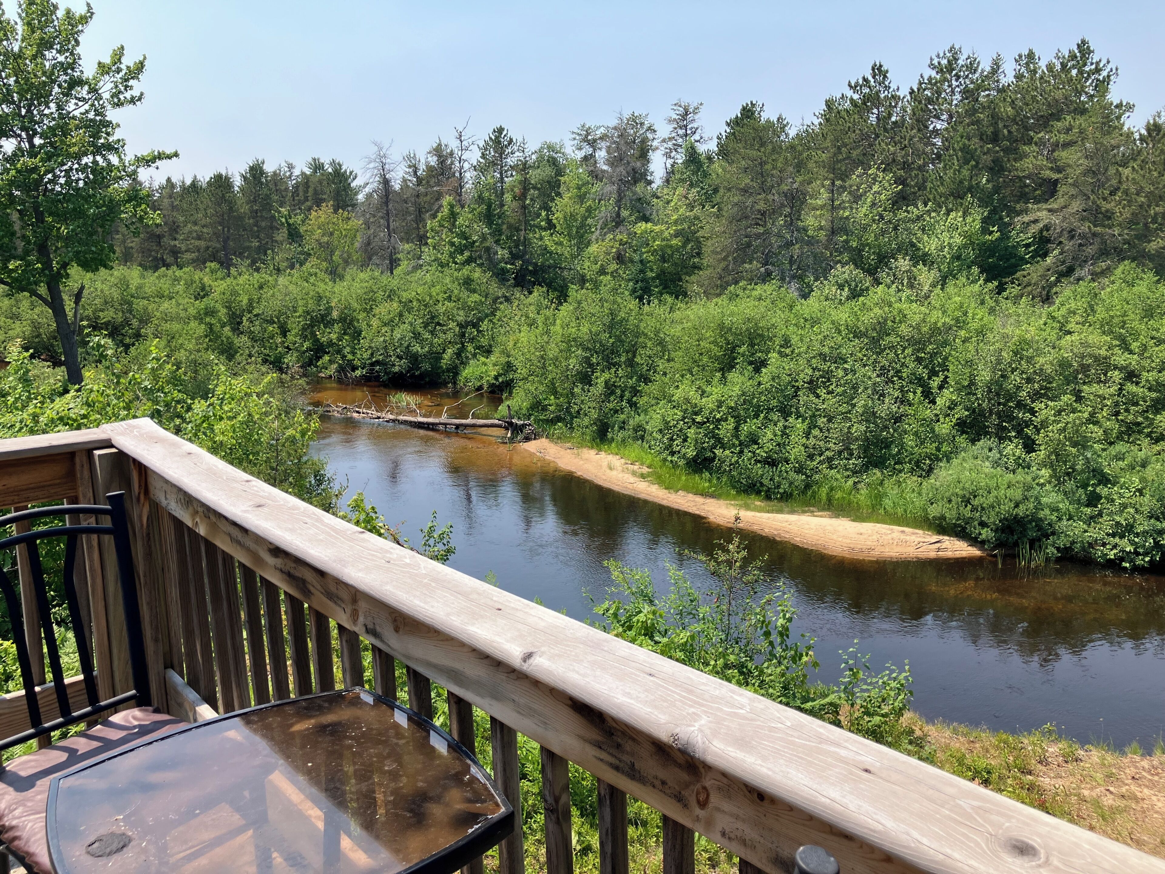 A wooden deck overlooking a river with dense greenery and trees.