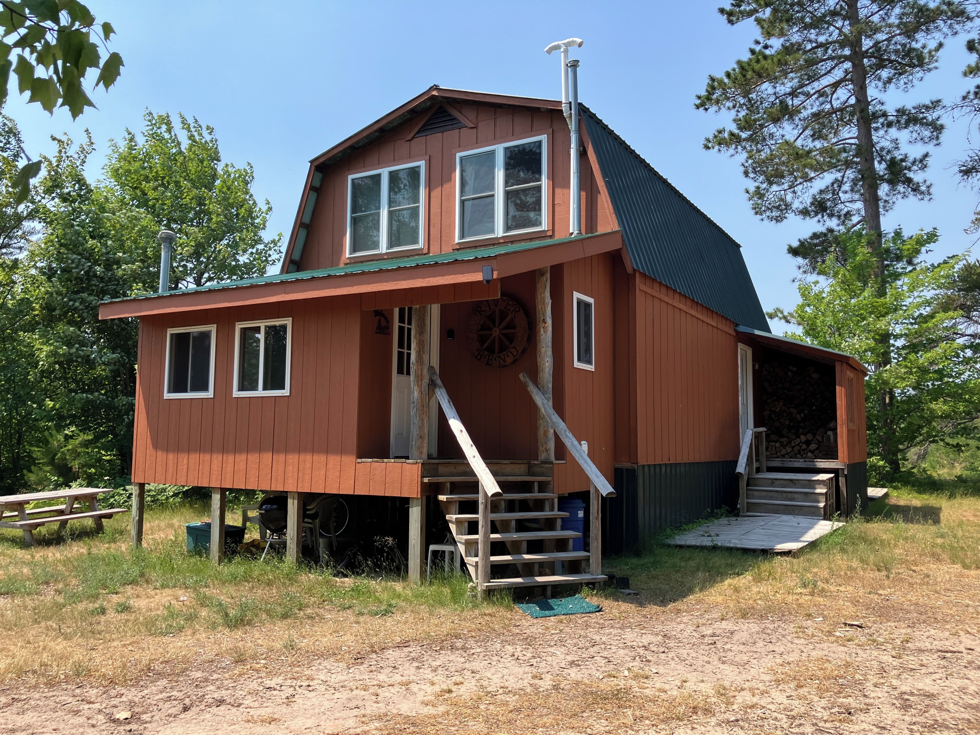 A wooden cabin with a steep roof, a porch, and a staircase leading to a loft area.