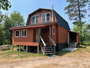 A wooden cabin with a steep roof, a porch, and a staircase leading to a loft area.