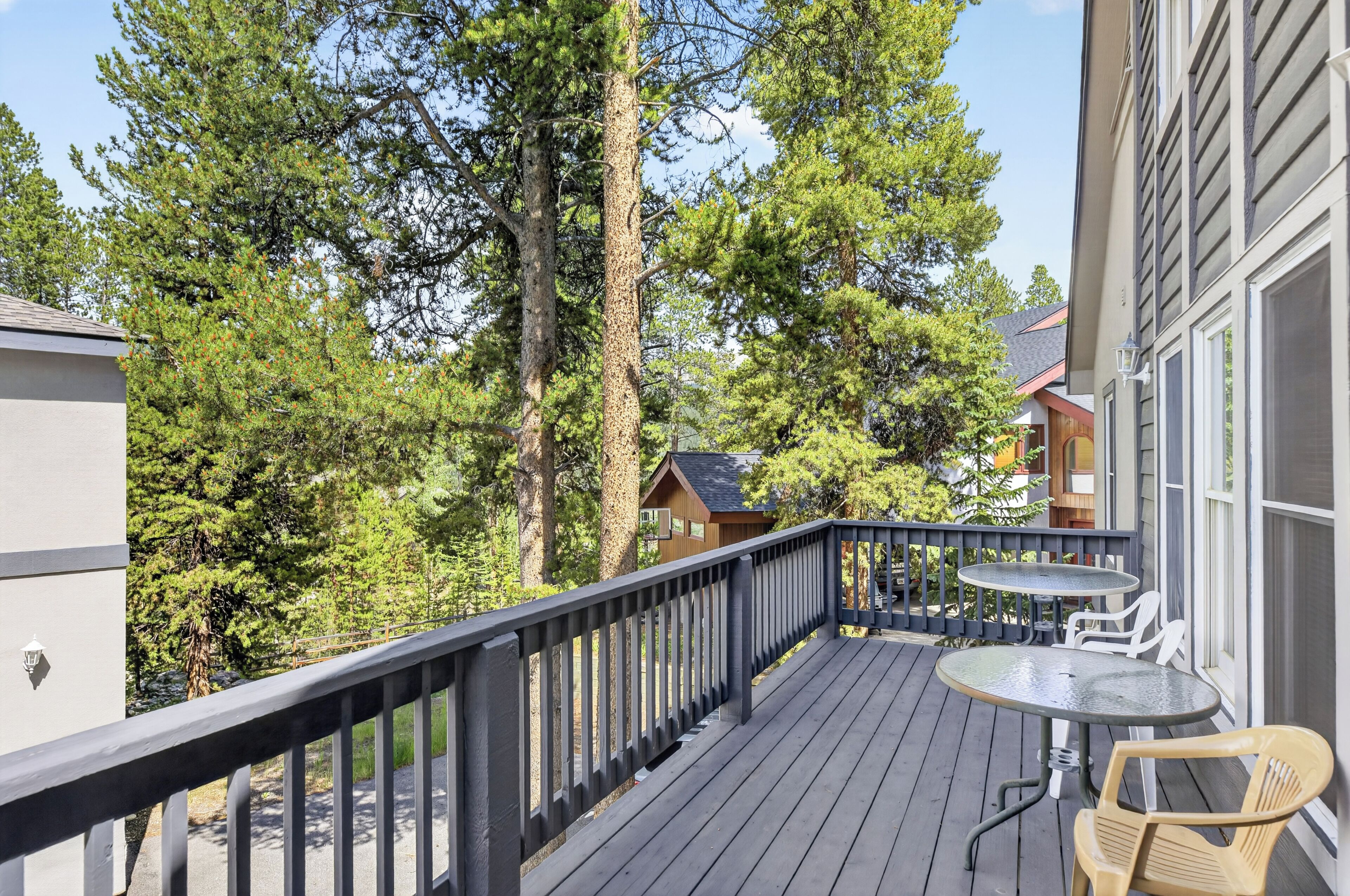 A wooden deck with a table and chairs, surrounded by trees and a building.