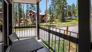 A balcony with a wicker chair and a view of a forested area with buildings. - NEW - Charming 2-Bedroom Condo Near Shuttle Stops and Downtown (Breckenridge)