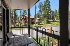A balcony with a wicker chair and a view of a forested area with buildings. - NEW - Charming 2-Bedroom Condo Near Shuttle Stops and Downtown (Breckenridge)