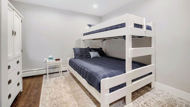 A bunk bed room with a white wardrobe, a small bedside table with a clock, and a patterned rug. - NEW - Charming 2-Bedroom Condo Near Shuttle Stops and Downtown (Breckenridge)