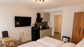 A hotel room with a bed, a desk, a chair, a television, a kitchenette, and a wardrobe.