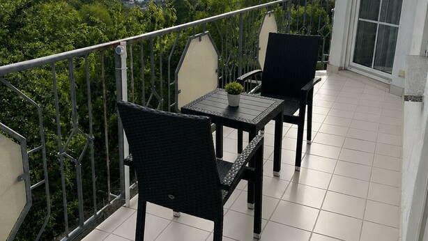 A balcony with two chairs and a table, overlooking a green landscape with hills.