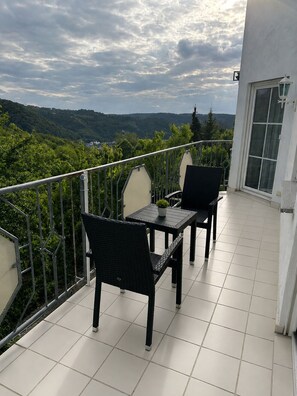 Un balcón con dos sillas y una mesa, con vistas a un paisaje verde y colinas.