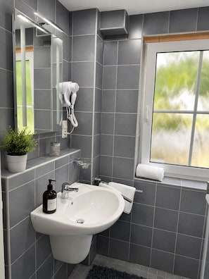 A modern bathroom with a large sink, a mirror, a towel rack, and a window.