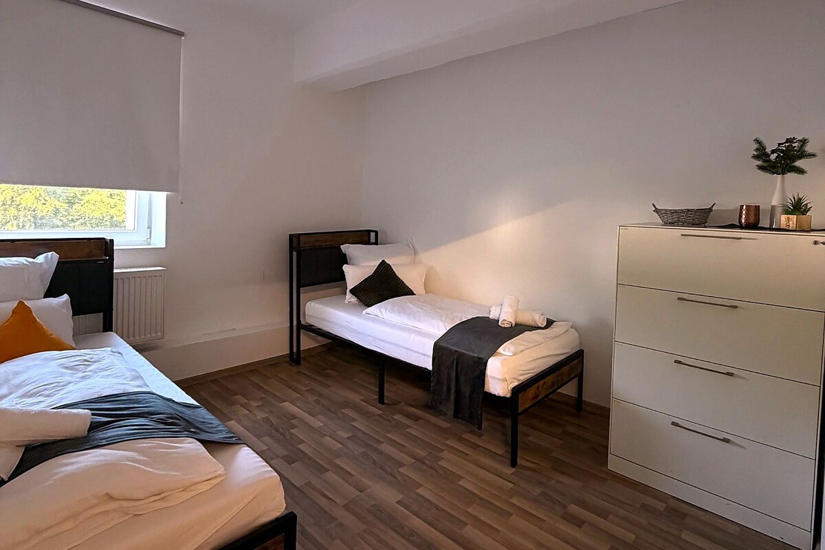 A bedroom with two beds, a dresser, and a window.