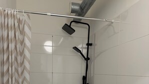 A shower area with a showerhead, a handheld showerhead, and a shower control panel.