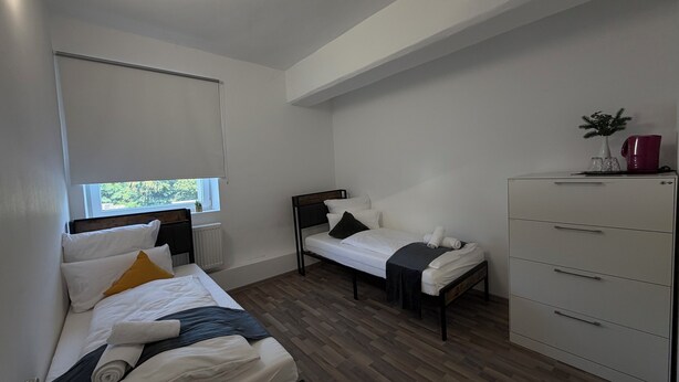 A room with two beds, a dresser, and a window.