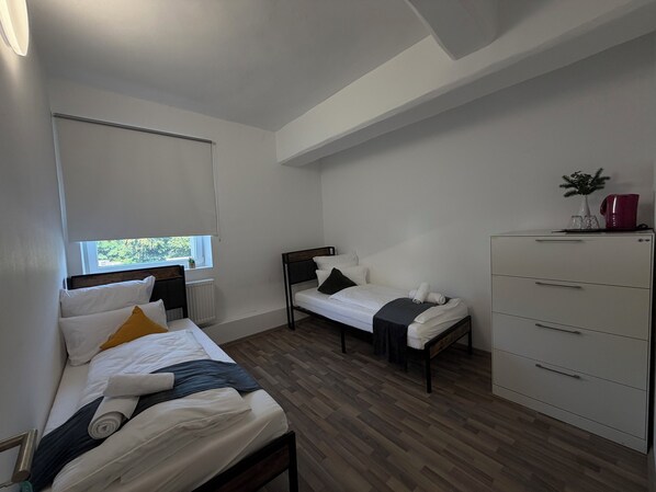 A room with two beds, a dresser, and a window.