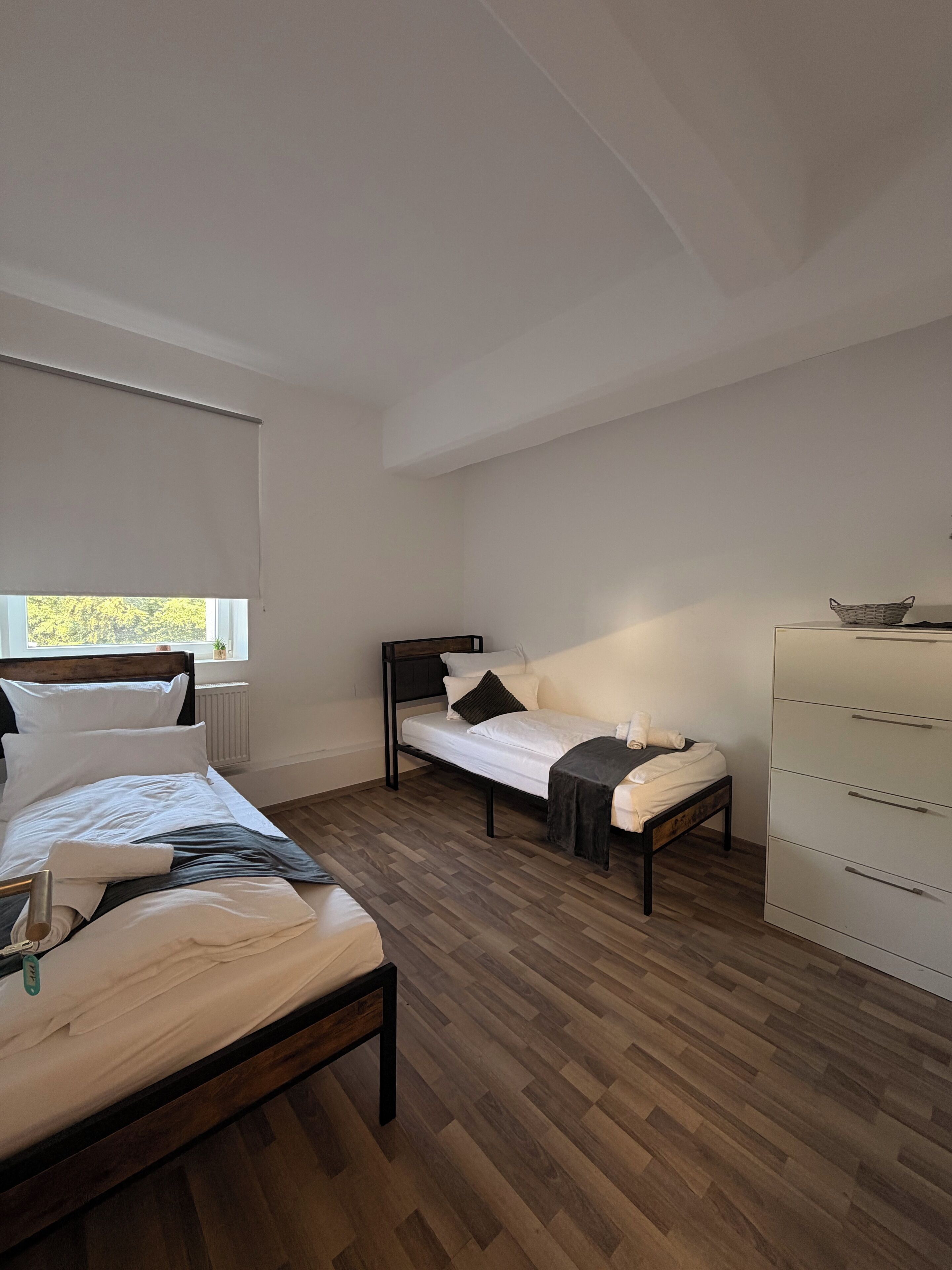A bedroom with two beds, a dresser, and a window.