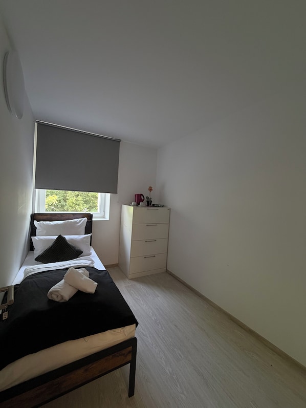 A bedroom with a bed, a bedside table, a dresser, and a window with a blind.