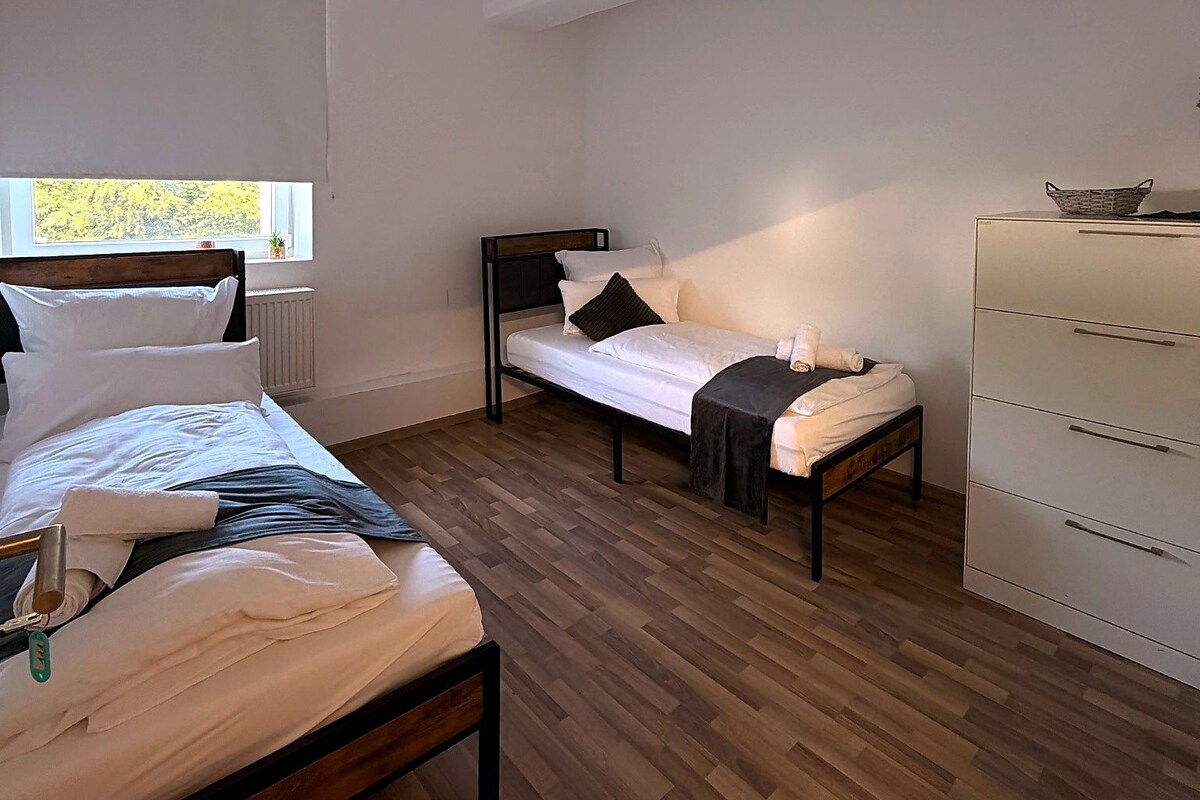 A bedroom with a bed, a bench, a dresser, and a window.