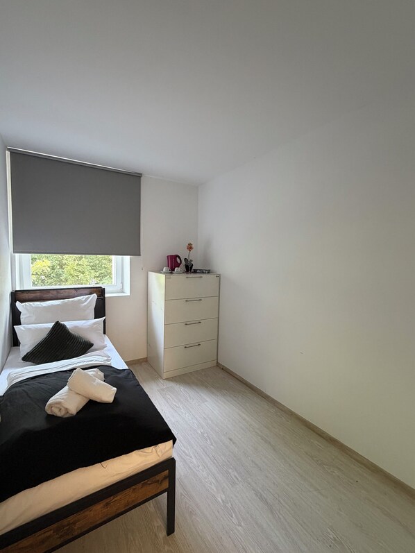 A bedroom with a bed, a dresser, a window with a blind, and a view of greenery outside.