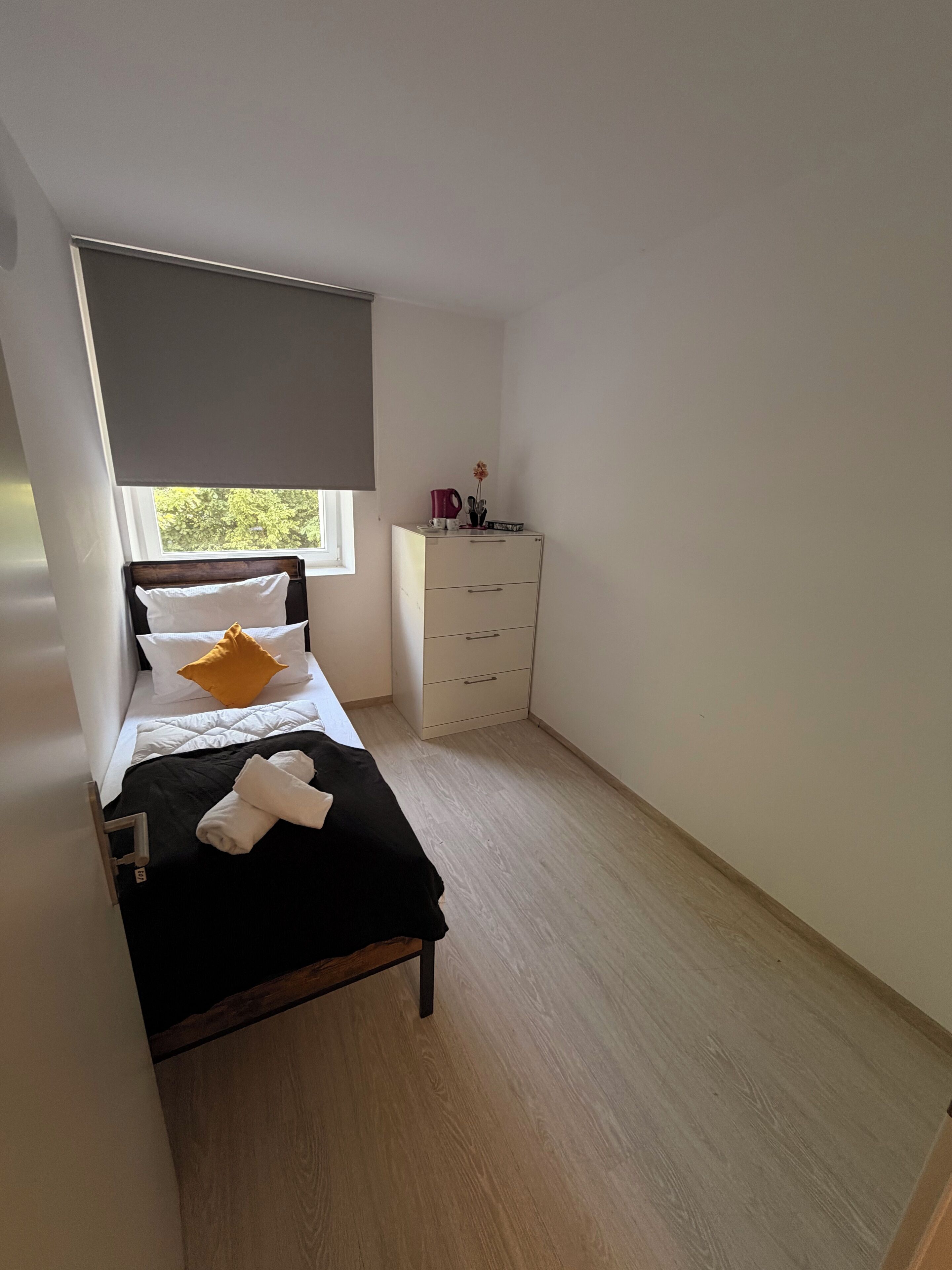 A bedroom with a bed, a nightstand, a dresser, and a window.